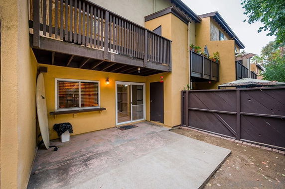 Rear view of a multi-story townhouse with a balcony and fenced backyard area.