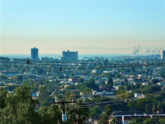 Panoramic view of a cityscape with buildings, cranes, and ocean in the background.