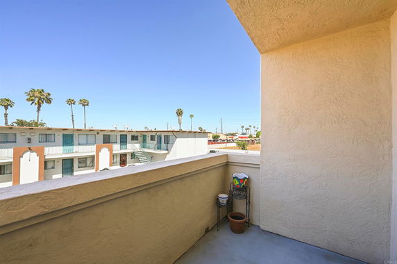 View from a balcony overlooking an apartment complex with visible rooftops and palm trees.