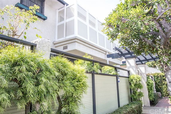 Front view of a multi-story building with a fenced balcony and greenery.