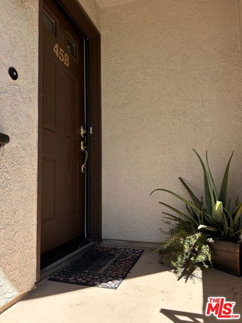 Front view of a house door with number 458, featuring a welcome mat and potted plant.