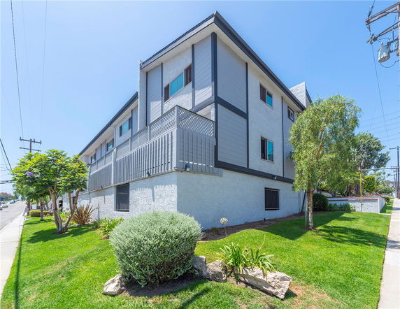 Front view of a multi-story residential building with balconies and a landscaped front yard.