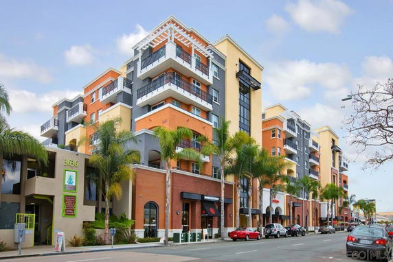 Front view of a multi-story apartment building with balconies and commercial spaces on the ground floor.