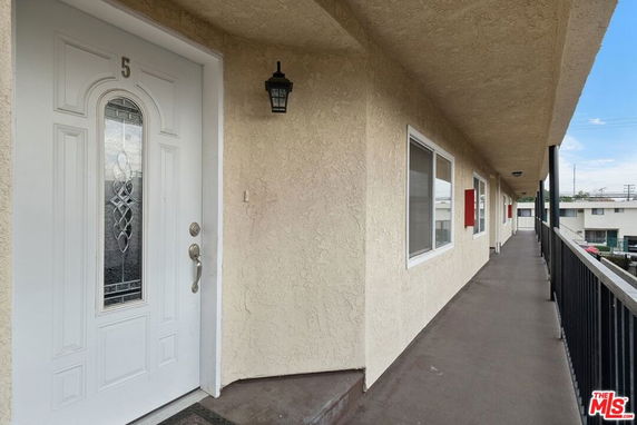 Exterior corridor of a building with numbered door and railing.