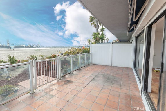 View of a beach and skyline from a balcony with glass railings and tiled floor.