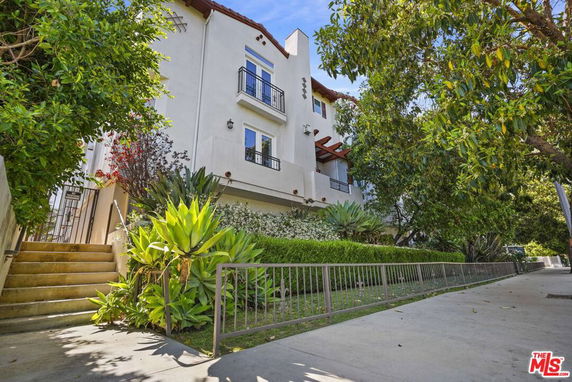 Front view of a multi-story residential building with balconies and stairs, surrounded by lush greenery.