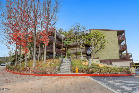 Front view of a multi-story residential building with balconies and surrounding trees.