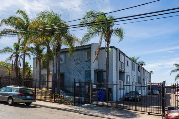 Front view of an apartment building with palm trees and a gated entrance.