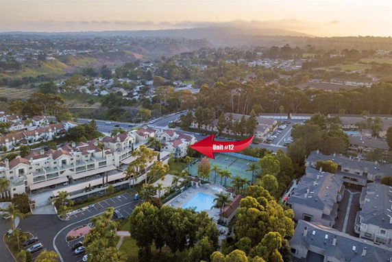 Aerial view of a residential complex with multiple buildings, swimming pool, tennis court, and surrounding greenery.