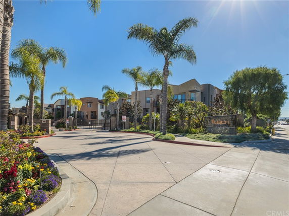 Front view of a residential complex with palm trees and a gated entrance.