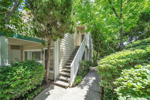 Exterior view of a two-story house with a staircase leading to the upper level, surrounded by trees and greenery.