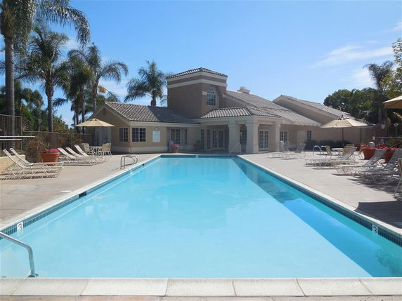 Outdoor swimming pool in front of a building with lounge chairs and umbrellas.