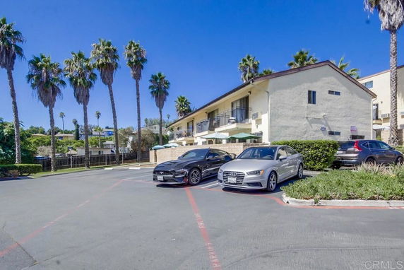 Outdoor parking area with several parked cars and palm trees in the background.