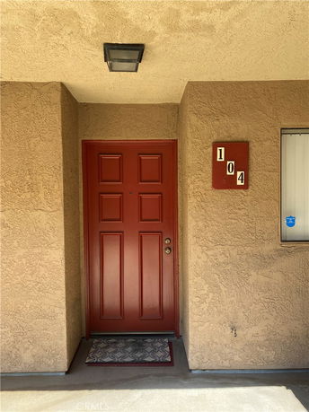 Front view of a red door with a unit number 104 on a beige exterior wall.
