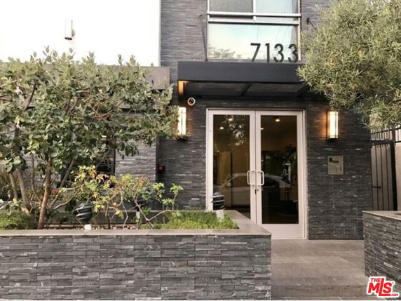 Front view of a modern building entrance with stone facade and glass doors.