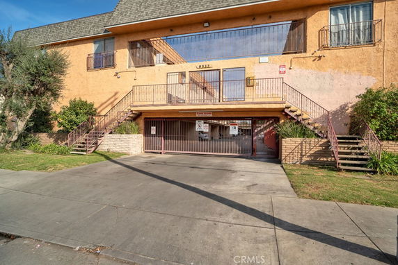 Front view of a two-story apartment building with external staircases and a gated entrance.