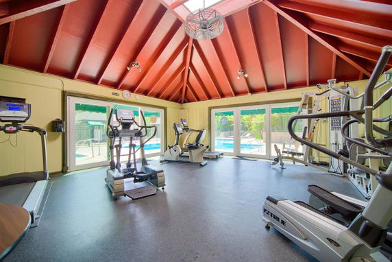 Indoor gym area with exercise equipment and large windows overlooking a pool.