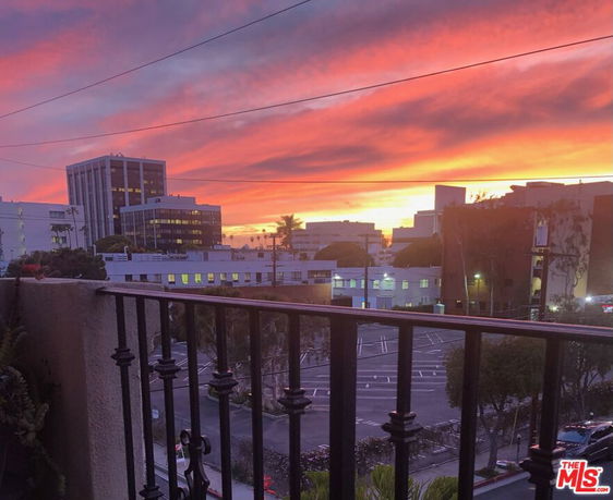 Panoramic view of a cityscape with a colorful sunset sky seen from a balcony.
