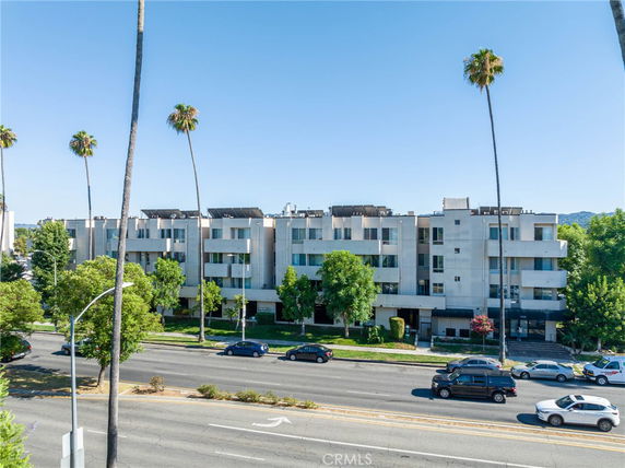 Front view of a multi-story apartment building with balconies and palm trees in front.