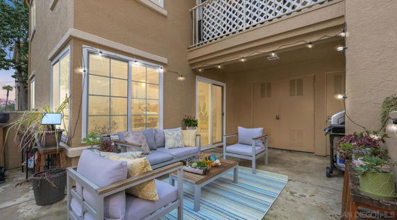 Outdoor patio area with seating and plants, adjacent to a house with large windows and sliding doors.