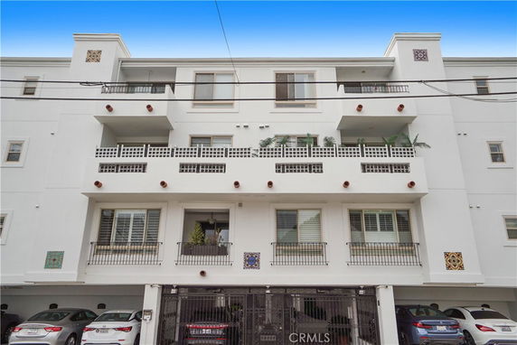 Front view of a multi-story residential building with balconies and parking area at the ground level.