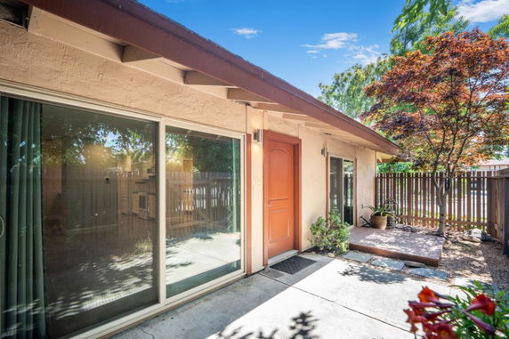Front view of a single-story house with large sliding glass doors and a wooden fence.