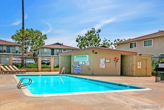 Outdoor swimming pool in a residential area with a fenced perimeter and poolside chairs.