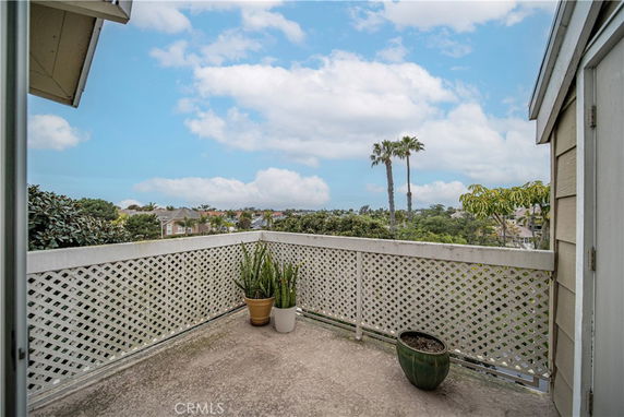 View from a balcony showing surrounding areas with trees, houses, and a clear sky.