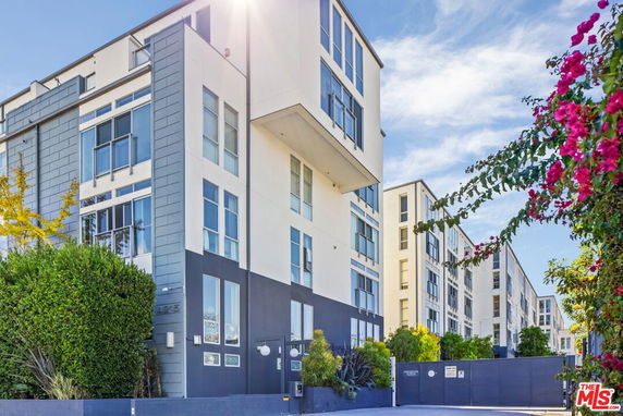 Front view of a modern multi-story apartment building with large windows and a gated entrance.