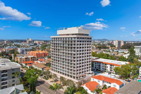 Aerial view highlighting a tall apartment building surrounded by smaller residential structures and a cityscape.