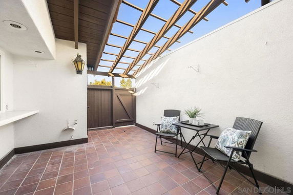 Outdoor patio area with tiled floor, chairs, and table under a wooden pergola.