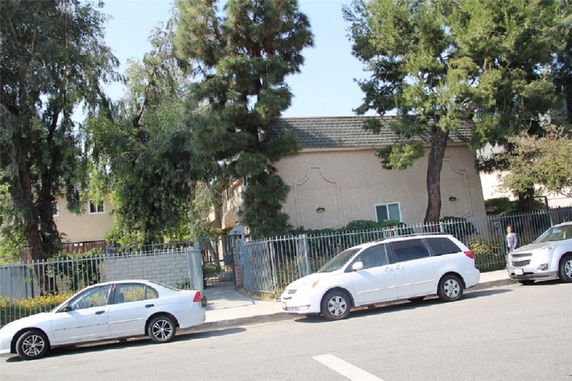 Front view of a house with a fence and multiple parked cars.