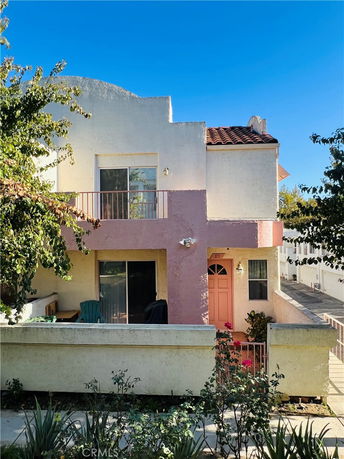Front view of a two-story house with a small balcony and a pink entrance door.