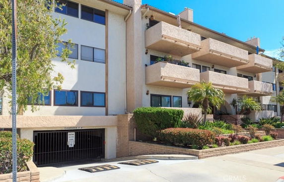 Front view of a multi-story apartment building with balconies and an underground parking entrance.