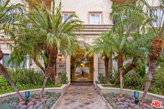 Front view of a building entrance with palm trees and a stone walkway.