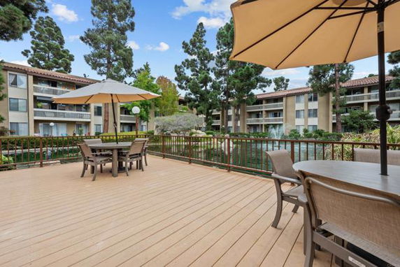 View of an apartment complex surrounded by trees, as seen from a wooden deck area with patio furniture and umbrellas.