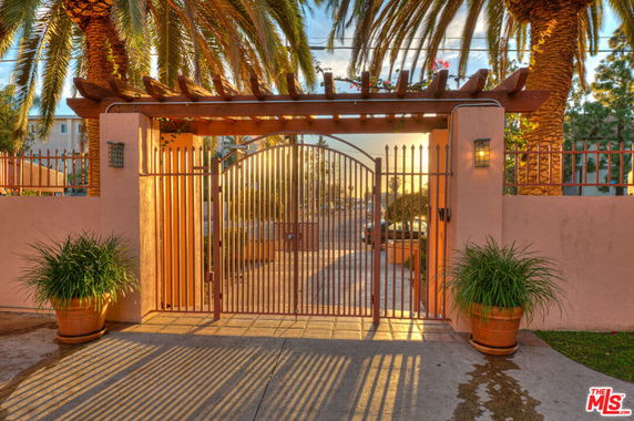 Front view of a gated entrance with a pergola and potted plants.