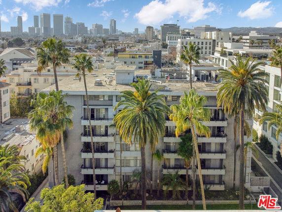 Front view of a multi-story residential building with balconies and palm trees.