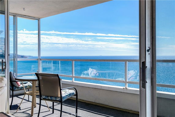 View of the ocean from a balcony with chairs and a glass railing.