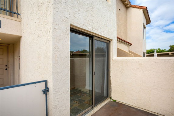 Exterior view of a beige stucco building with a sliding glass door and a small patio area.