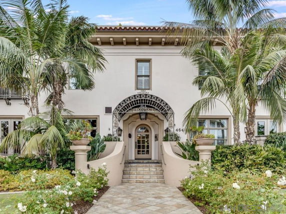 Front view of a two-story house with an arched entrance and surrounding palm trees.