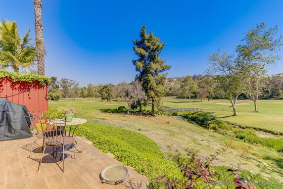 Outdoor patio area overlooking a green golf course with trees and a small bridge in the distance.