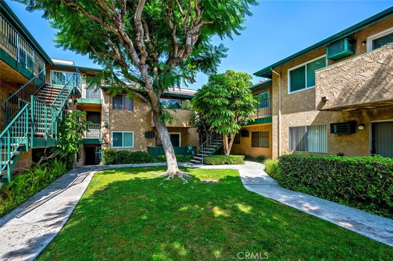 View of an apartment complex with multiple levels and staircases, surrounded by greenery and trees.