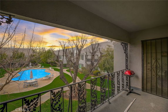 View from a balcony overlooking a swimming pool and surrounding buildings at sunset.