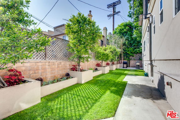 View of a building's backyard area with grass, trees, and a concrete path.