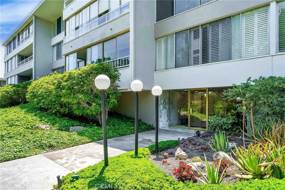 Front view of a multi-story building with glass entrance and surrounding greenery.