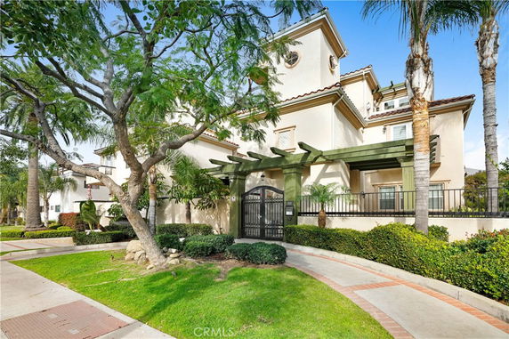 Front view of a multi-story residential building with decorative greenery and a gated entrance.