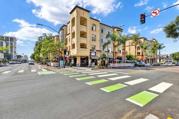 Street view of a multi-story building with shops on the ground floor and balconies on the upper floors.