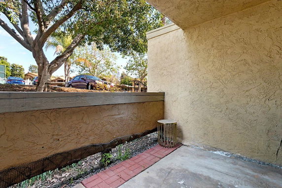 Partial view of an outdoor area with a wall, trees, and parked cars.