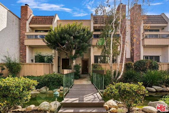 Front view of a multi-story house with balconies and a small bridge over a pond.